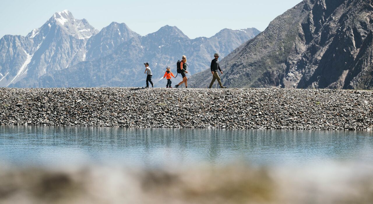 Familie wandert auf einem Kiesweg vor der Bergkulisse des Stubaitals